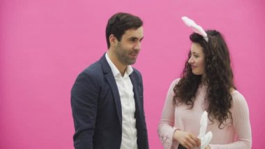 Genç pembe bir arka plan üzerinde duran çift. El tavşan kulakları tutarak ve aşık kocasıyla seyir karısı başında, pembe tavşan. Mutlu aile Paskalya için hazırlanıyor.