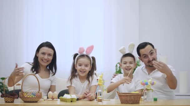 Familia feliz y alegre: madre, padre y dos niños sonríen ampliamente y comparten sus emociones positivas en el fondo blanco. La familia invita amablemente a pasar un rato divertido con ellos mostrando un gesto — Vídeos de Stock