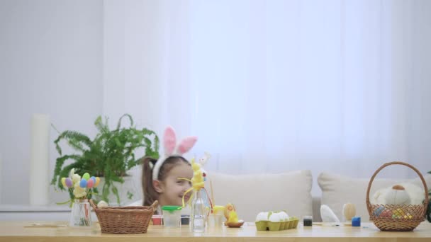 Kleine spelen kinderen met bunny oren op hun hoofd verstop onder de houten tafel, vol met Pasen decoraties. — Stockvideo