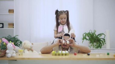 Mutlu ve neşeli kızı onun babaları omuzlarında oturan ve dans. Babası ahşap masa altında oturan birkaç renkli boyalar olduğu. Tavşan kulaklı oynak baba tutuyor