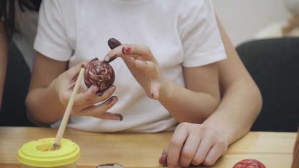 Un petit garçon en T-shirt blanc est en train de colorer un œuf de Pâques dans ses mains. Père l'aide, repérant une peinture rouge sur l'œuf de Pâques . — Video