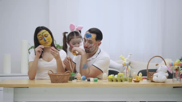 Cute couple is colorizing Easter eggs. Their daughter says stands on the sofa, behind parents and scare them. Childish couple came back to childhood. Laught in the room. — Stock Video