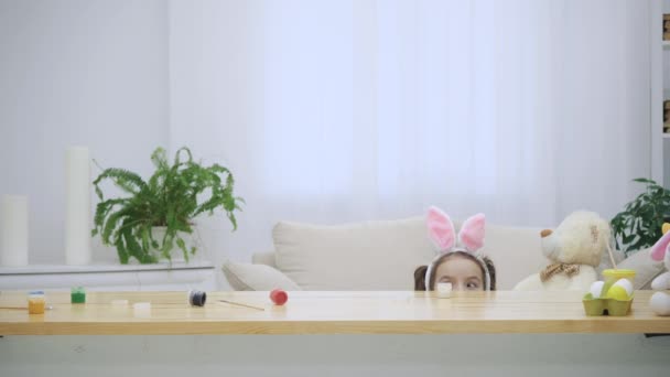 Kleine spelen jongen met bunny oren op hun hoofd verbergt onder de houten tafel, vol met Pasen decoraties. Schattig meisje is met haar grappige vader uitkijken. Thery rush in een dikke knuffel aan het einde — Stockvideo
