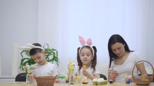 La familia se concentra y hace artesanía, coloreando los huevos de Pascua. De repente, el padre entra y señala con el dedo, atrayendo la atención de las familias . — Vídeo de stock