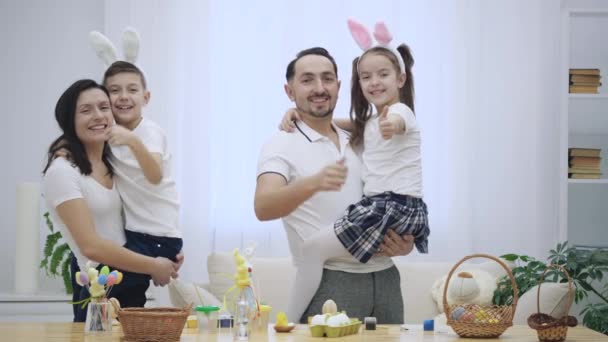 Happy and cheerful family: mother, father and two kids are smiling widely and share their positive emotions on the white background. Parents are holding their children on their hands. High five all — Stock Video