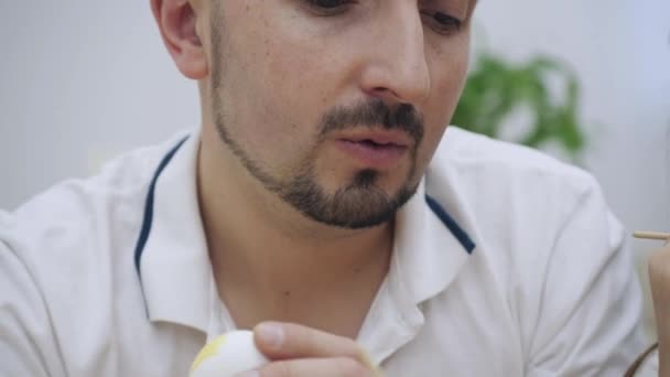 La niña linda se está divirtiendo coloreando un huevo de Pascua con una ayuda de pincel en color azul. Su padre está coloreando un huevo de Pascua en un color amarillo, y su hijo en un color chocolate . — Vídeos de Stock