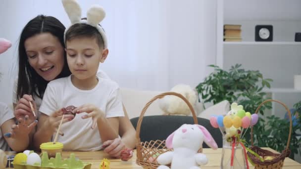 Menino bonito com orelhas de coelhinhos está sentado de joelhos em suas mães e mostra suas unhas pintadas. Mãe está pintando suas filhas unhas em vermelho com um pincel de tinta . — Vídeo de Stock