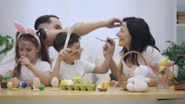 Ebeveynleri onların neşeli ve sevimli çocukları ile her diğer, ahşap tablo Easter süslemeleri tam oturan colourizing. Babası hanımları alnına renklendirme yapıyor. Oğlu katılır ve mu