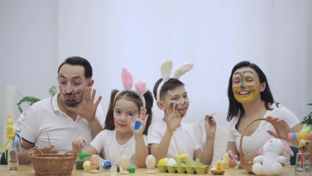 A fürge és a kis gyerekek, szülők is colourized egymást, ül a fából készült asztal, tele a húsvéti dekoráció. Családi kedves hullám és a hüvelykujj ujjai fel Térkép, és sok más — Stock videók