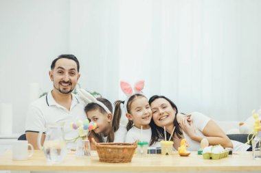 Mutlu aile Paskalya için hazırlanıyor gülümseyerek. Baba oğul hugs, anne kızı hugs. Tavşan kulakları çocuklarda. Bir sürü tatil küçük şey masada.