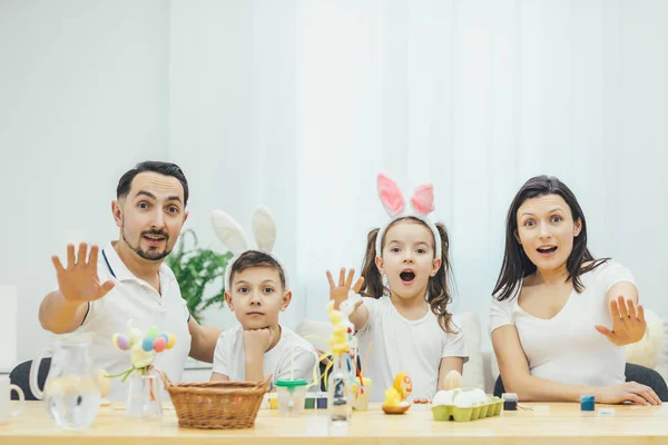 Emotional easter family sitting at the table extending their hands forward, showing stop sign. Open mouthes, expressiveness on their faces.