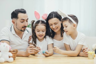 Dostu aile birlikte masada oturan kardeşim ve kız kardeşi bunny kulaklar. Şirin çocuk mavi bir yumurta, herkes dostça boyama boya fırçası ile bu Paskalya yumurtası düzenliyor.