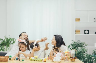 Baba ve iki sevimli küçük çocuk anneler yüzlerini renk karar verdi. Kız ve erkek kardeş tavşan kulakları giyiyor. Rahat bir ortam.