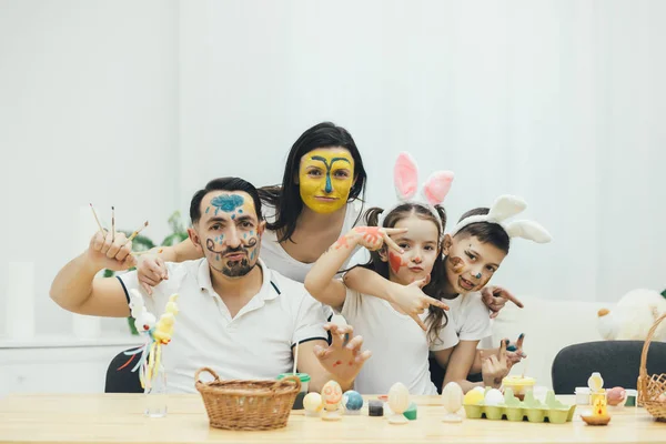 Creative family, children in bunny ears. Everyone with colored faces. They are extremely happy and demonstrate it to the camera, smiling and posing comically. — Stock Photo, Image