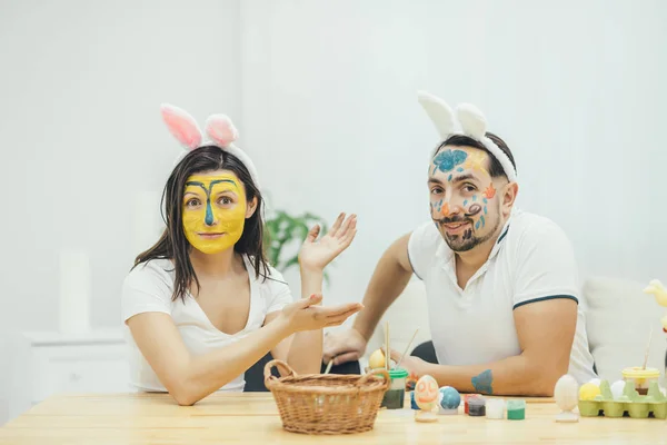 Mother and father painted their faces instead of easter eggs. They are looking at the camera with childish face expression. Foolish behavior. Paint and color. — Stock Photo, Image