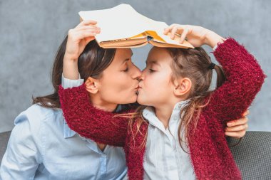 Anne ve kızı gri bir arka plan üzerinde. Öpüşme kucaklama ve kız öğrenci anneler başkanı ve onun açık kitap tutarak.