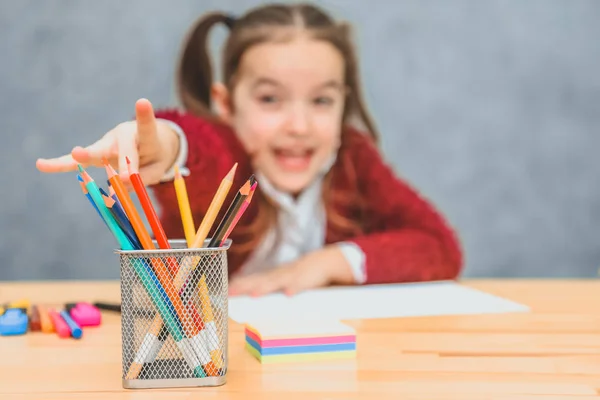 Primer plano concepto de lápices multicolores sobre la mesa en el fondo de la amante de la chica. Una colegiala extendiendo su mano elige el lápiz correcto. Fondo gris . — Foto de Stock