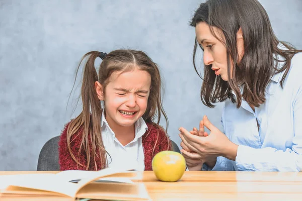 Annem bebeğiyle konuşuyor. Bu gri bir arka plan üzerinde sırasında. Kız ağlıyor, anne elini okşuyor ve kızıyla konuşuyor. Gri arka plan. Kitabın masasında ve yeşil bir elma. — Stok fotoğraf