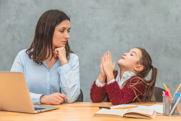 Young mother and schoolgirl on a gray background. My daughter hands up asking my mother to look at the laptop. During this, the mother has a confused look. On a gray background.