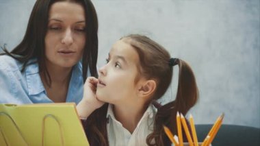 Anne ve kızı gri bir arka plan üzerinde masada oturuyor. Bu okuma sırasında, kitaplar, gülümsemeler, sarılmalar. İlişkiler kavramı.
