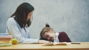 Gri arka plan üzerinde bir kız sandalyenin arkasına başını koyarak masada oturur. Bu esnada annem kızına gülümsüyor. İlişkiler kavramı.