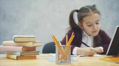Akıllı, özenli kız öğrenci masada otururken ev ödevi yapar. Bu yazı sırasında, kalem sarı bir renk alır.