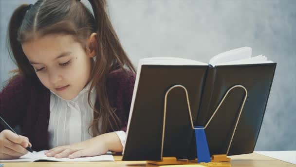 Een slim schoolmeisje zit aan tafel en voert een huiswerkopdracht uit. Gedurende deze tijd kijkt hij in een Zwartboek. — Stockvideo