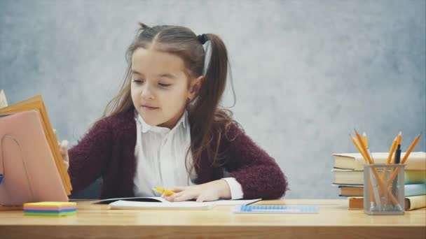 Ein intelligentes Schulmädchen sitzt am Tisch und schreibt Hausaufgaben. während dieser Suche wird die Seite im Buch durchsucht — Stockvideo