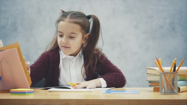 Una colegiala inteligente se sienta a la mesa y escribe los deberes. Durante estas búsquedas la página en el libro — Vídeo de stock