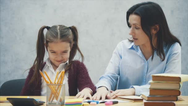 Mooie schoolmeisje zittend aan de tafel. Maakt huiswerk met haar moeder thuis. — Stockvideo