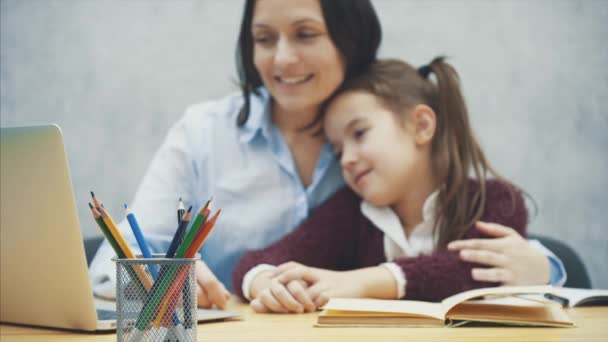 お母さんと娘はテーブルの上で灰色のノートパソコンを見て抱き合う。このぼやけた背景の間に。人間関係と愛の概念. — ストック動画