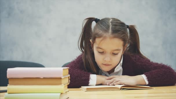 Egy iskolás lány ül a szürke háttér. Ez idő alatt a tanuló olvassa a könyvet figyelmesen. Szorgalmas diák Reading alszik. — Stock videók
