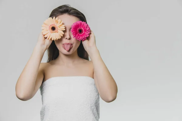 One gorgeous girl in white towel with two flowers, which have different colors. She shows her tongue.