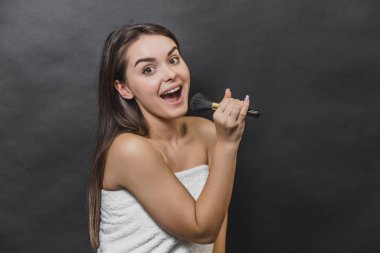 Makyaj fırçası tutan beyaz havlu güzel kız. Şarkı söylüyor..