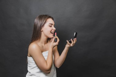 Genç güzel kız kırmızı ruj ile dudaklarını boyar. Cilt bakım konsepti. Aynaya bakmak.