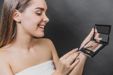 Güzel genç kız siyah bir arka plan üzerinde duruyor. Bu esnada göz farı sizin elinizde tutulur. Oldukça temiz bir cilde sahiptir.