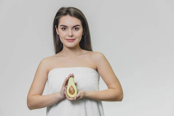 Retrato de chica bonita sosteniendo la mitad del aguacate en las manos mirando en cámara sobre fondo blanco . —  Fotos de Stock