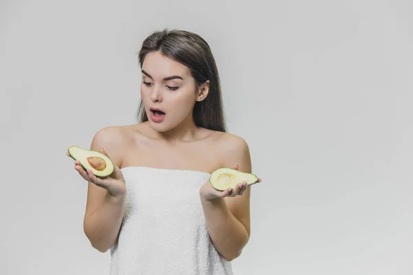 Retrato de mujer joven con piel limpia y pura sosteniendo aguacate en las manos. Cara asombrada. Mirando hacia abajo . —  Fotos de Stock