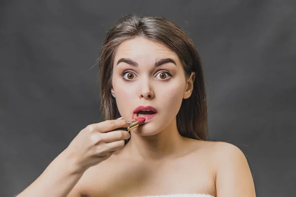 Belle jeune fille se tient sur un fond noir. Pendant ce temps, le rouge à lèvres est peint avec du rouge à lèvres . — Photo