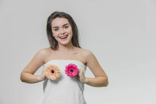 Młoda piękna dziewczyna w białym ręczniku. Uśmiecha się i trzyma kwiaty w dłoniach. — Zdjęcie stockowe