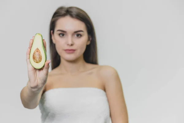 Seriøs vakker jente med avokado i hvitt håndkle. Avocado er i fokus . – stockfoto