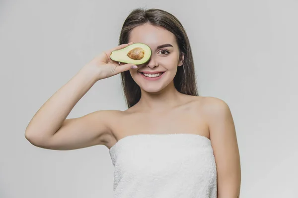 Joven chica hermosa en toalla blanca con medio aguacate. Ella sonríe . —  Fotos de Stock