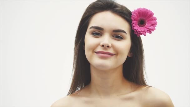 Όμορφο νεαρό όμορφο κορίτσι απομονώνεται σε λευκό φόντο. Με ένα ροζ λουλούδι στα μαλλιά, τα συναισθήματα, τα καλλυντικά. — Αρχείο Βίντεο
