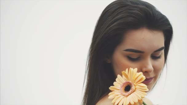 Retrato de una hermosa joven con una flor sobre un fondo blanco. Mira en diferentes direcciones . — Vídeos de Stock