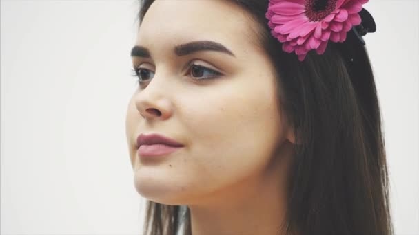 Hermosa joven hermosa chica aislada sobre fondo blanco. Con una flor rosa en el cabello, emociones, cosméticos . — Vídeo de stock