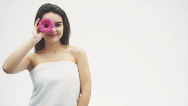 Young pretty girl standing on a white background. During this raising the flower closes it with one eye and looks at the camera. — Stock Video