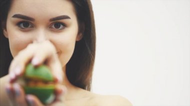 Beyaz bir arka plan üzerinde duran iyi bir genç kız. Sağlıklı bir çekici esmer bir avokado parçacığı elinde tutar ve dikkatle her yarısında inceler.