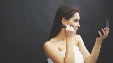 Siyah bir arka plan üzerinde duran genç güzel kız. Bu esnada, aynaya bakan bir fırça ile tüm yüze toz döker..