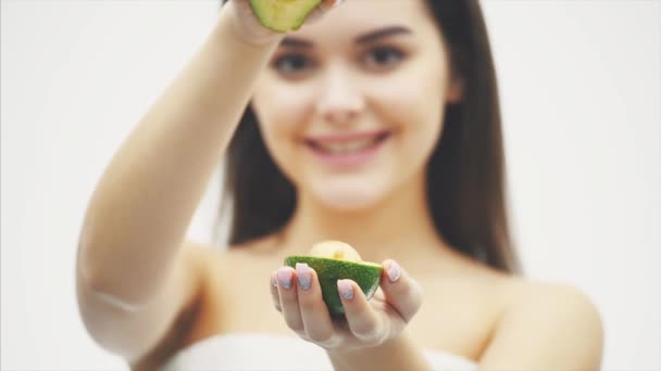 Una buena joven de pie sobre un fondo blanco. Una morena atractiva y saludable sostiene en sus manos una partícula de aguacate sobre un fondo borroso de chicas . — Vídeos de Stock