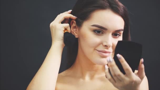Närbild porträtt ung vacker flicka som tittar i spegeln och håller makeup borstar i höger hand. — Stockvideo
